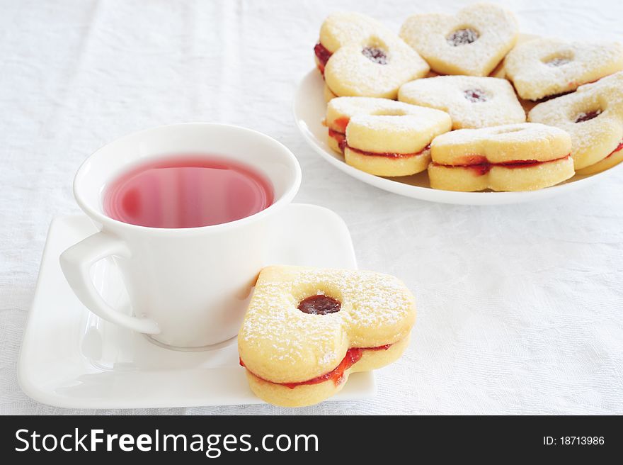 Fruit tea in a white cup and cookies in the shape of hearts on a white tablecloth. Fruit tea in a white cup and cookies in the shape of hearts on a white tablecloth