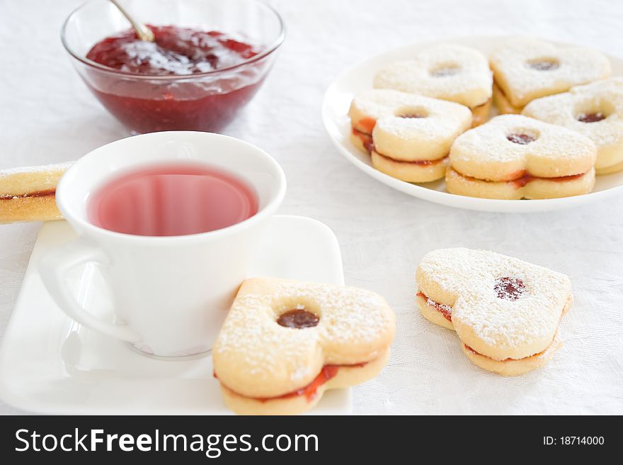 Fruit tea in a white cup, jam piala and cookies in the shape of hearts on a white tablecloth. Fruit tea in a white cup, jam piala and cookies in the shape of hearts on a white tablecloth