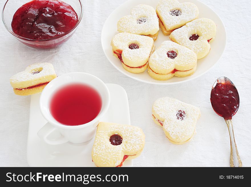 Fruit tea in a white cup, jam piala and cookies in the shape of hearts on a white tablecloth. Fruit tea in a white cup, jam piala and cookies in the shape of hearts on a white tablecloth