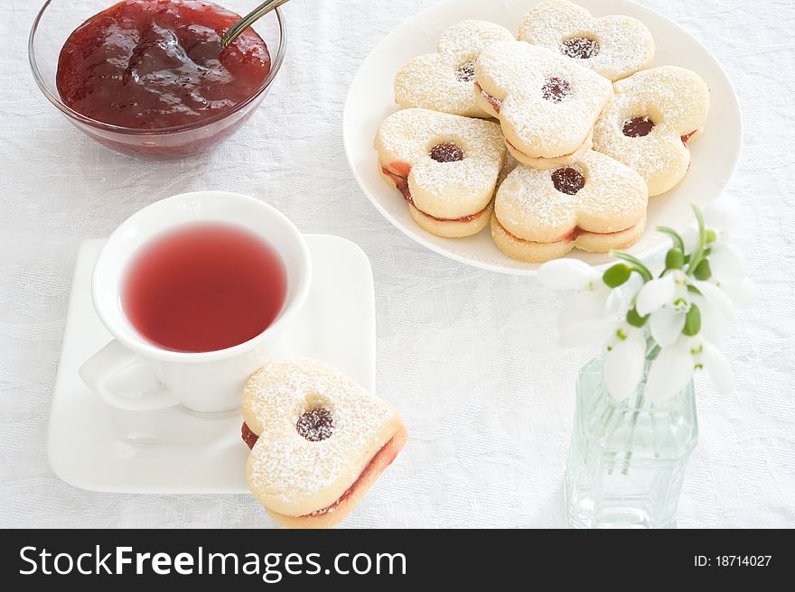 Fruit tea in a white cup, jam piala and cookies in the shape of hearts on a white tablecloth. Fruit tea in a white cup, jam piala and cookies in the shape of hearts on a white tablecloth