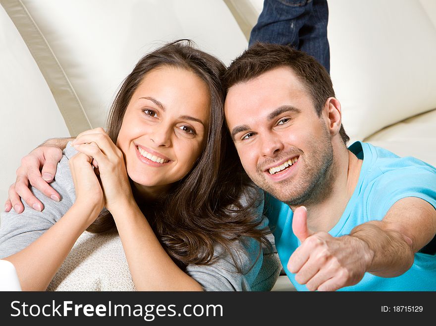 Young embracing couple on white sofa, boyfriend shows thumbnail. Young embracing couple on white sofa, boyfriend shows thumbnail