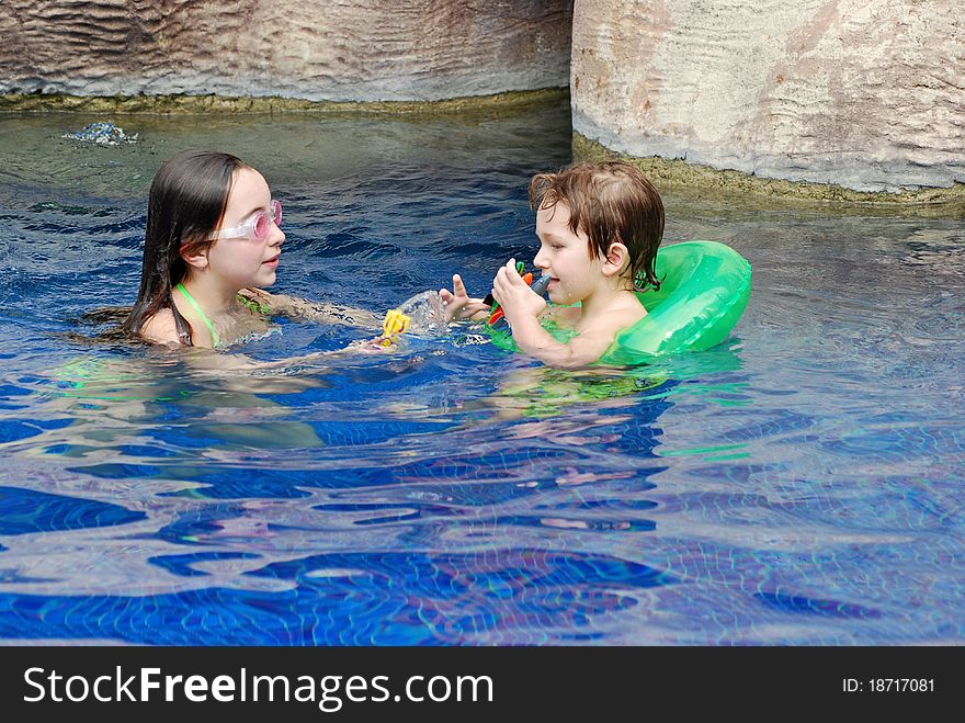 A boy and girl, brother and sister, in the pool playing together while the younger one wears a green float. A boy and girl, brother and sister, in the pool playing together while the younger one wears a green float.