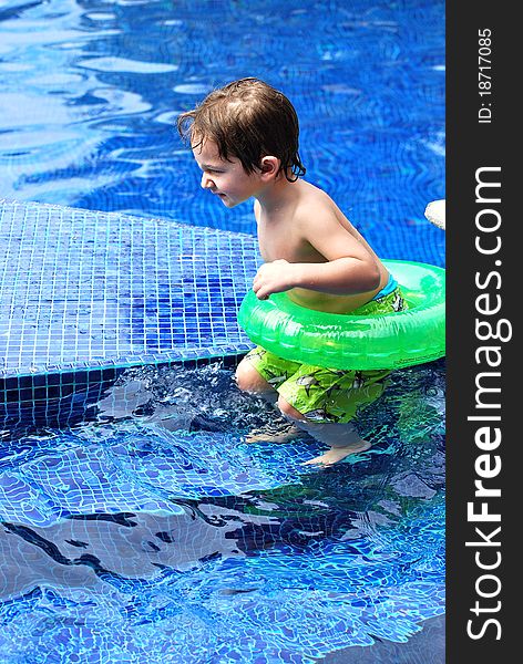 A white caucasian toddler boy about to jump from the steps into the blue tile pool with his green blown up inner-tube float. A white caucasian toddler boy about to jump from the steps into the blue tile pool with his green blown up inner-tube float.