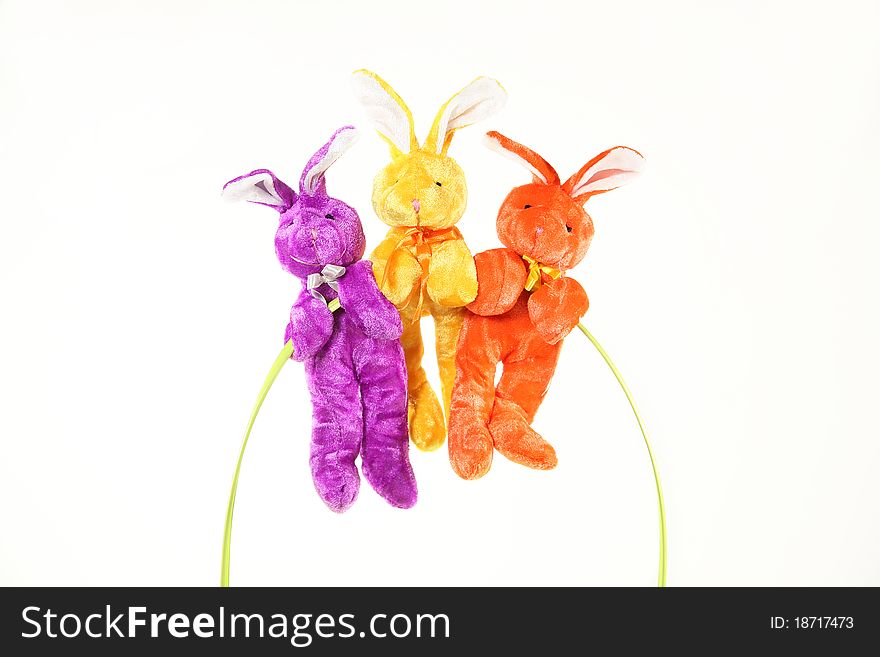 Three vibrant, colorful bunnies hang from handle of Easter basket with Sample text against white background. Three vibrant, colorful bunnies hang from handle of Easter basket with Sample text against white background.