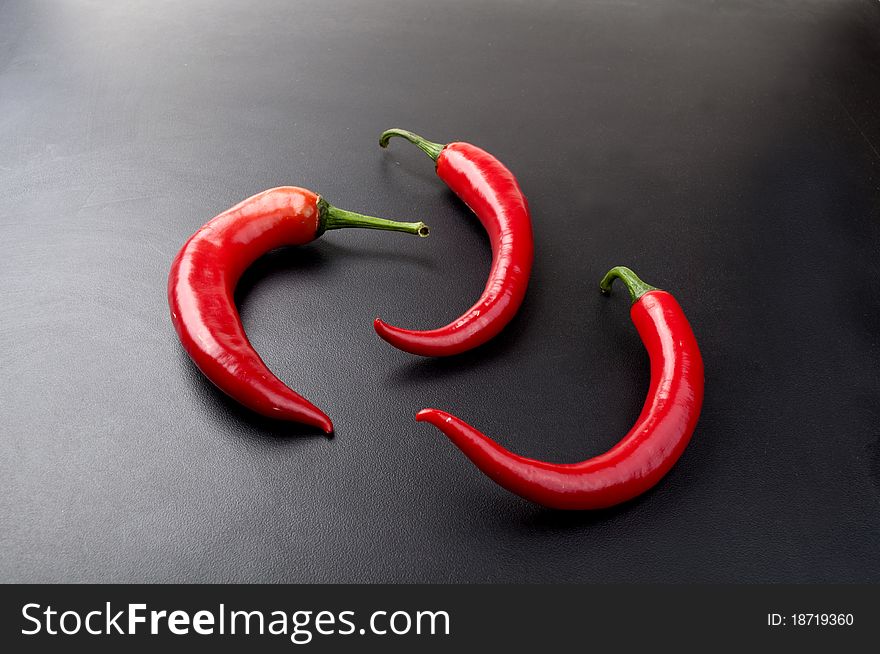 Three red pepper on a black background