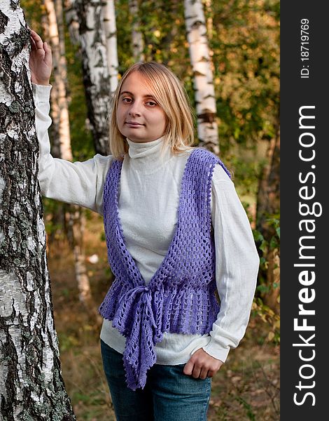 A girl in a lilac vest and white polo-neck sweater and jeans in a forest. A girl in a lilac vest and white polo-neck sweater and jeans in a forest