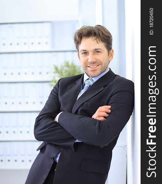 Young businessman standing in office lobby, using smartphone, smiling