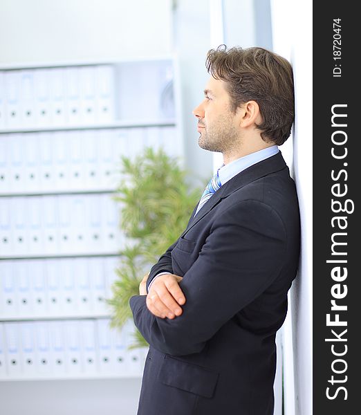 Young businessman standing in office lobby, using smartphone, smiling
