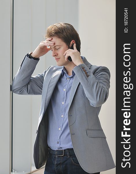 Young business man talk by cellphone over bright window in big hall