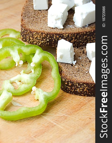 Feta cheese cubes with bread and pepper on wooden board