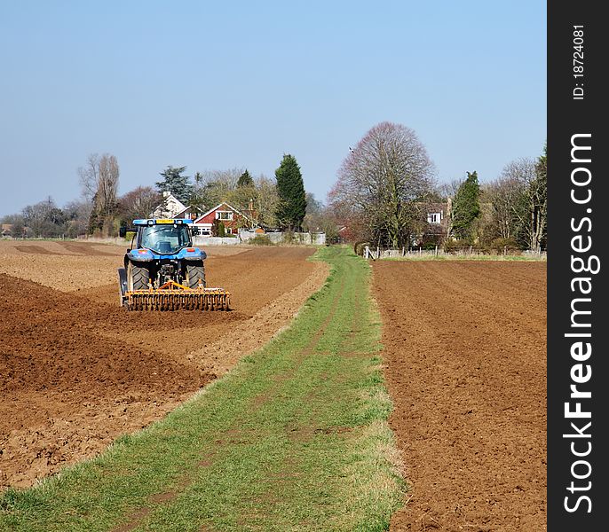 Tractor ploughing  in rural england with grassy track between fields. Tractor ploughing  in rural england with grassy track between fields