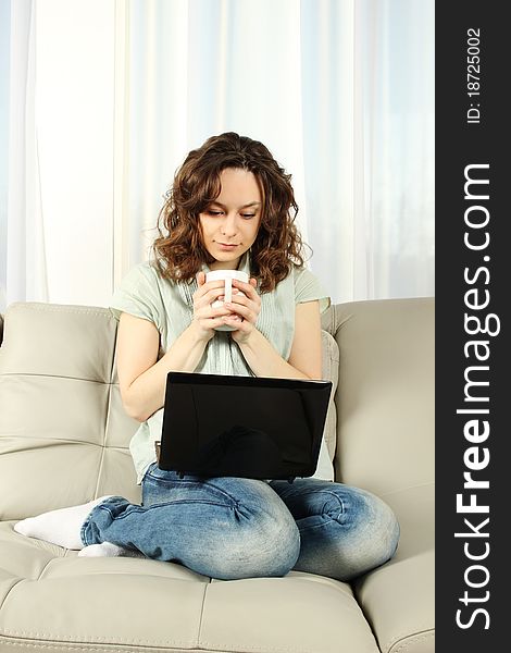 Young attractive woman sitting in a sofa with a cup of coffee and a laptop. Young attractive woman sitting in a sofa with a cup of coffee and a laptop