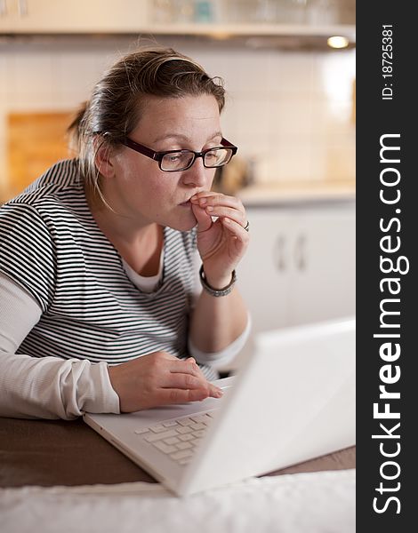 Woman sitting with her laptop in the kitchen with a worried expression. Woman sitting with her laptop in the kitchen with a worried expression