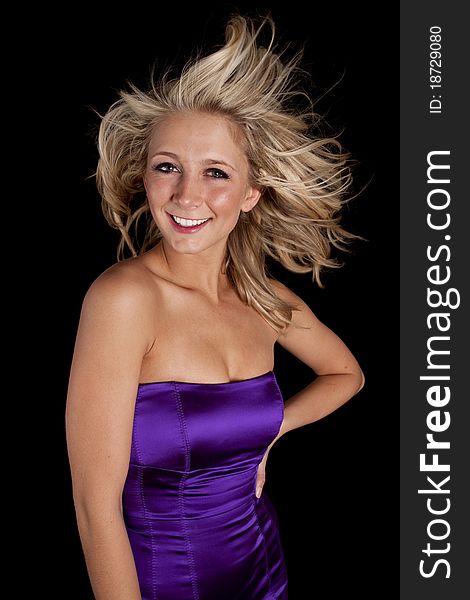 A woman in her purple dress standing in front of the black background with wind blowing in her hair. A woman in her purple dress standing in front of the black background with wind blowing in her hair.