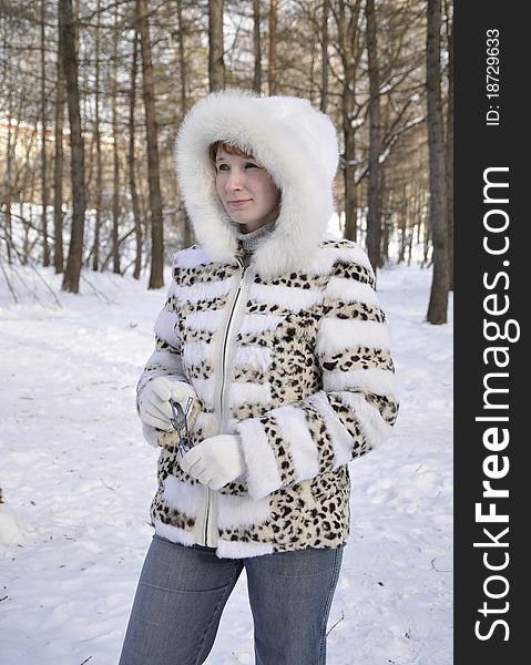 The young girl rejoices to the sun in the winter in a white fur coat with a fluffy hood
