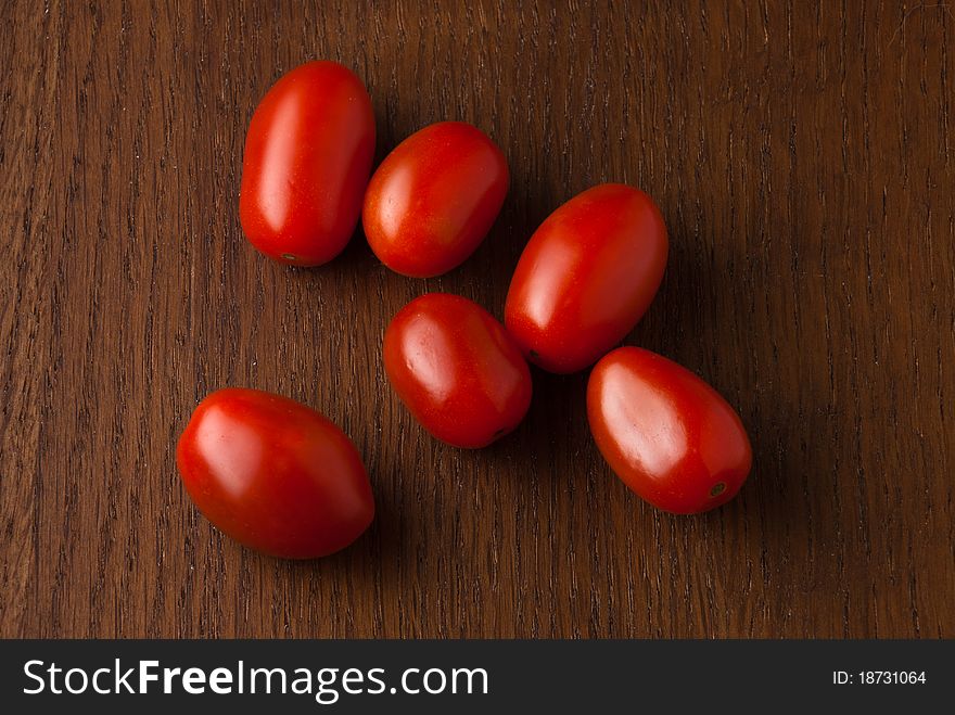 Six fresh crisp red cherry tomatoes on a wood grain table. Six fresh crisp red cherry tomatoes on a wood grain table.