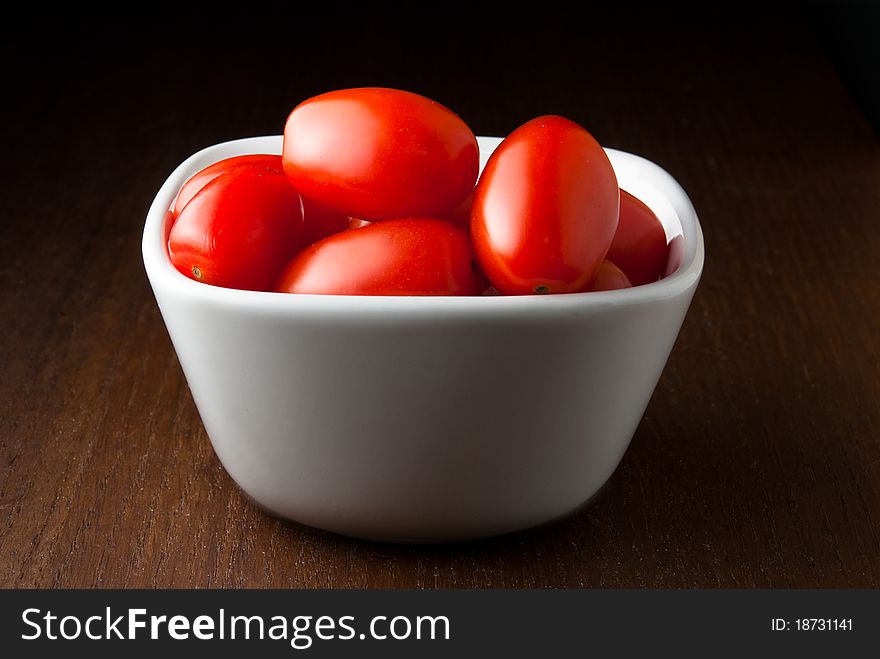 A bowl of cherry tomatoes on a wood table.