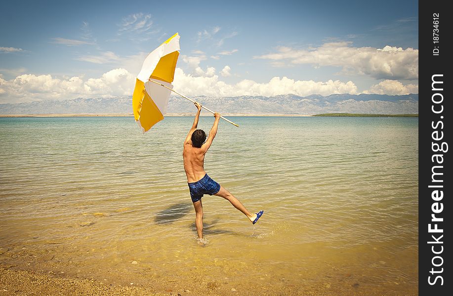 A happy young man on a beach holding a big open sun umbrella. A happy young man on a beach holding a big open sun umbrella