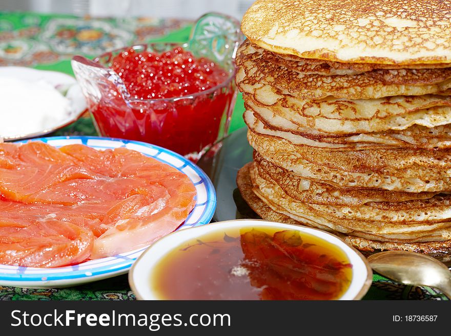 Studio photography of a pancakes with salmon, honey, caviar, cream on the table still life with unfocused background. Russian traditional food for the holidays maslenitsa