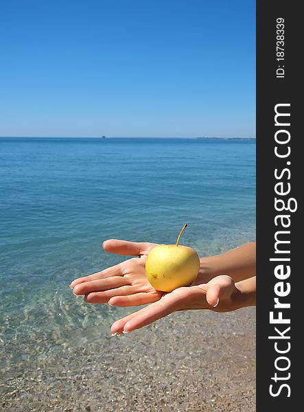 Woman hands giving a yellow apple with sea and sky background. Woman hands giving a yellow apple with sea and sky background