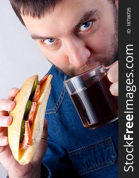 A man drinks tea from a glass cup and eating a delicious sandwich. A man drinks tea from a glass cup and eating a delicious sandwich