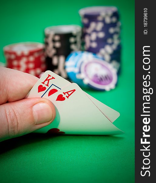 Poker chips and a hand flip the cards against green felt