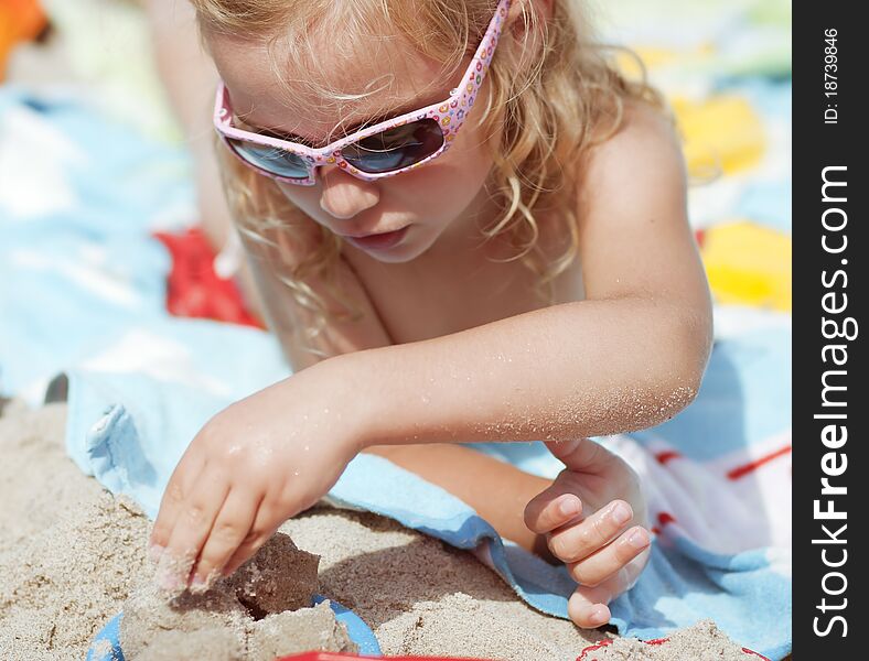 Little girl with sunglasses playing in the sand