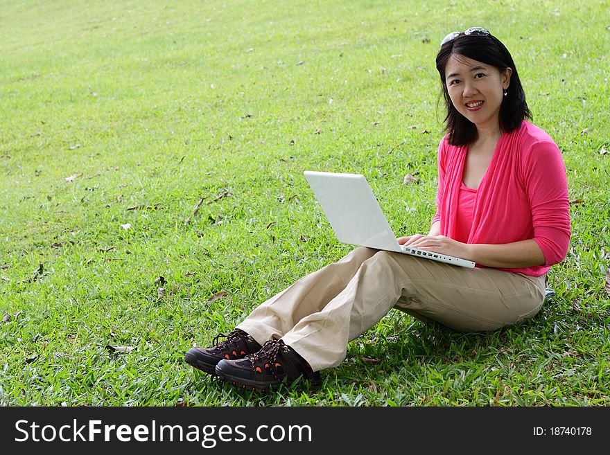 An Asian woman using her laptop at a park. An Asian woman using her laptop at a park