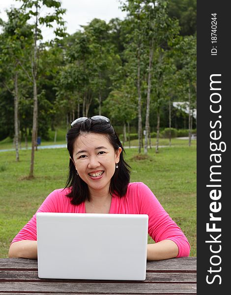 An Asian woman using her laptop at a park. An Asian woman using her laptop at a park