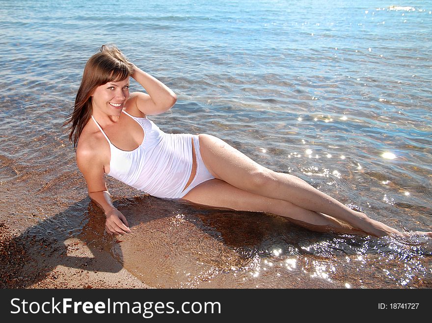 A beautiful young girl dressed in white sits at the water's edge on the beach and smiling. A beautiful young girl dressed in white sits at the water's edge on the beach and smiling