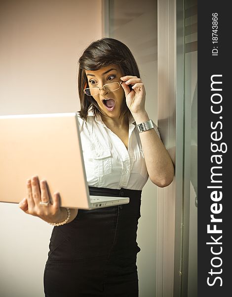 Woman with a laptop on her hand and grabing her glasses with the other hand and looking surprised by what she sees on the screen. Woman with a laptop on her hand and grabing her glasses with the other hand and looking surprised by what she sees on the screen.