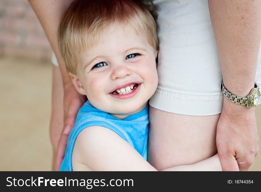 A cute little boy holding on to his Mother's legs, closeup with selective focus on face. A cute little boy holding on to his Mother's legs, closeup with selective focus on face