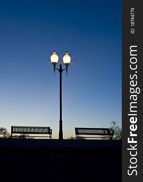 Park benches silhouetted against a darkening sky with lamps. Park benches silhouetted against a darkening sky with lamps