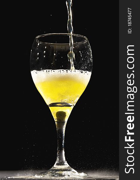 Yellow fizzling clear liquid being poured into champagne glass with a black background. . Yellow fizzling clear liquid being poured into champagne glass with a black background.