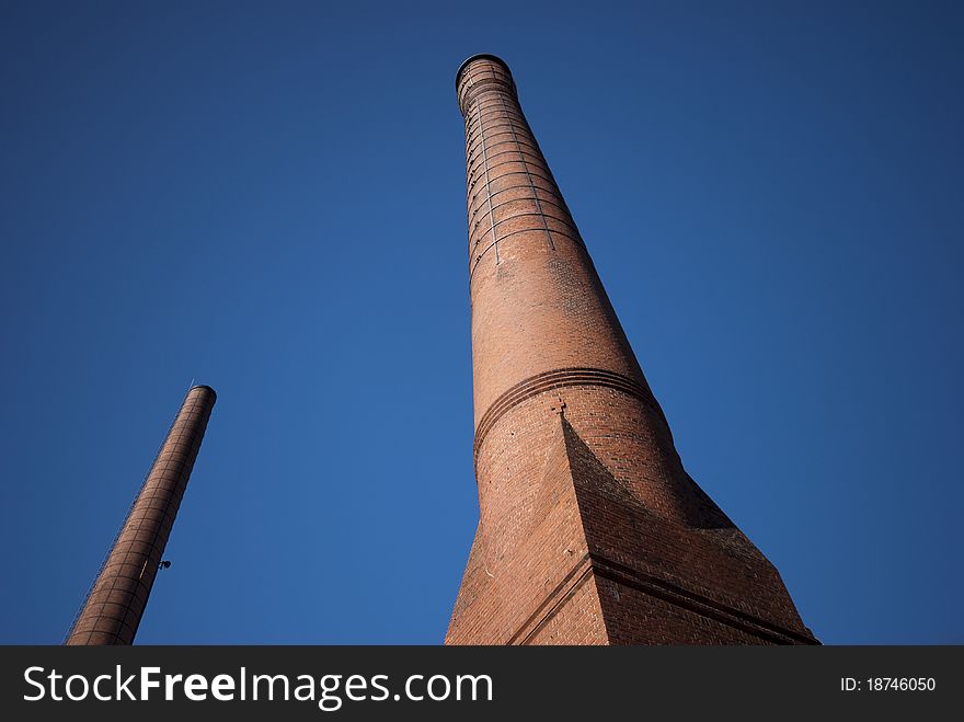 Two brick factory chimneys alone in the blue sky. Two brick factory chimneys alone in the blue sky.