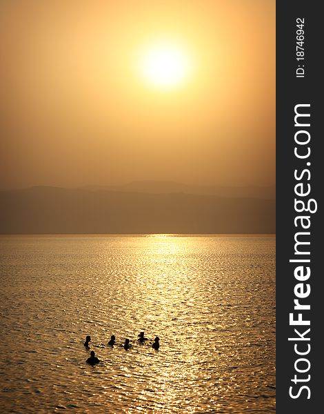 Tourists are enjoying the salty water of Dead Sea in a resort at the time of sunset. Coast of Israel on the background. Tourists are enjoying the salty water of Dead Sea in a resort at the time of sunset. Coast of Israel on the background.