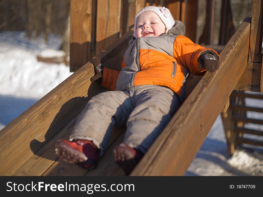 Adorable baby sliding from wooden baby slide in winter sunny park. Adorable baby sliding from wooden baby slide in winter sunny park