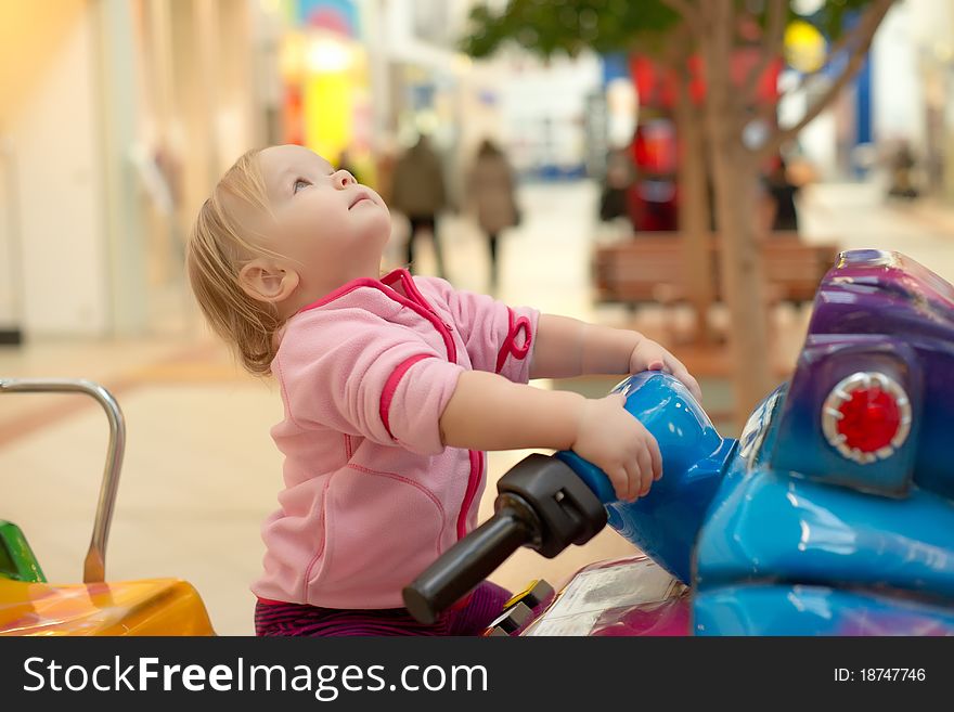 Young adorable baby ride on baby motorcycle in mall. Look up