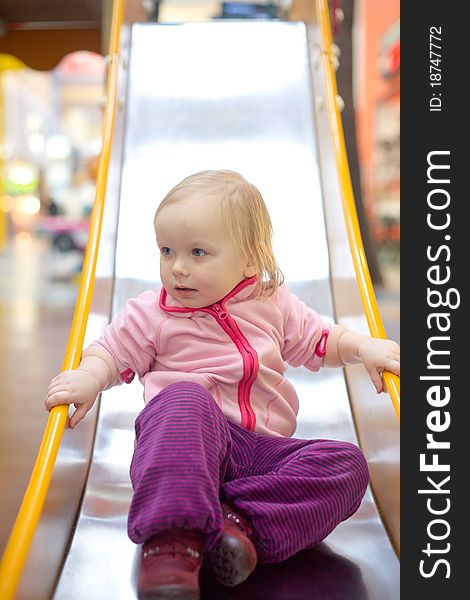 Young adorable baby sliding down baby slide on playground in mall. Sitting on the end of slide