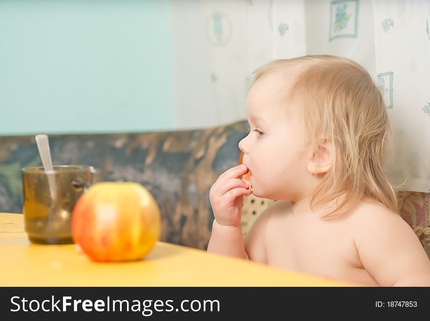 Adorable baby eat piece of bread while drink tea in kitchen. Adorable baby eat piece of bread while drink tea in kitchen