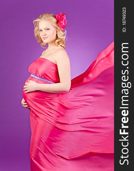 A young pregnant woman in a pink dress on the purple background. A young pregnant woman in a pink dress on the purple background