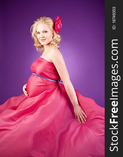 A young pregnant woman in a pink dress on the purple background. A young pregnant woman in a pink dress on the purple background