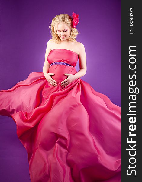 A young pregnant woman in a pink dress on the purple background. A young pregnant woman in a pink dress on the purple background