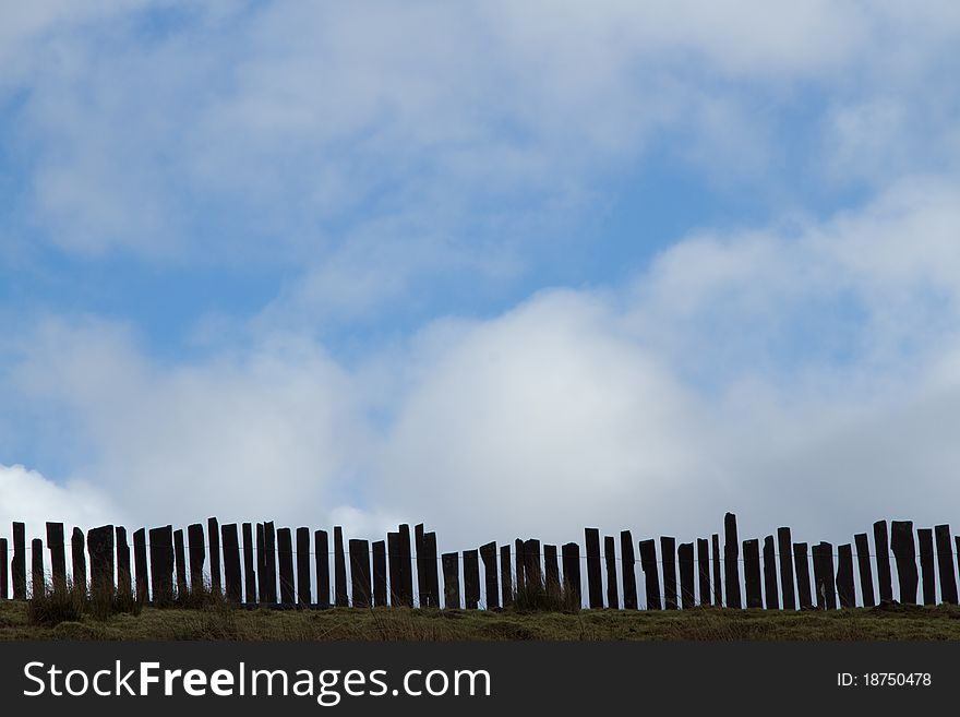 A traditional slate fence, irregular, with gaps on grass with tufts. A clody blue sky makes the background with space for consumer information. A traditional slate fence, irregular, with gaps on grass with tufts. A clody blue sky makes the background with space for consumer information.
