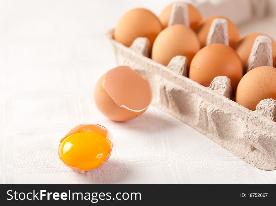 Broken brown egg beside a carton of ten eggs
