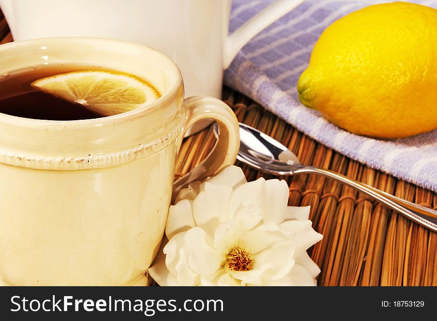 Cup of freshly brewed tea and lemon served with a white rose from the garden, focus on front rim of cup. Cup of freshly brewed tea and lemon served with a white rose from the garden, focus on front rim of cup