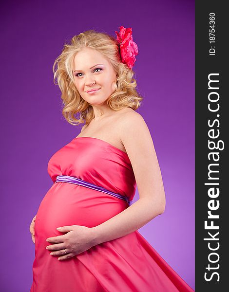 A young pregnant woman in a pink dress on the purple background. A young pregnant woman in a pink dress on the purple background