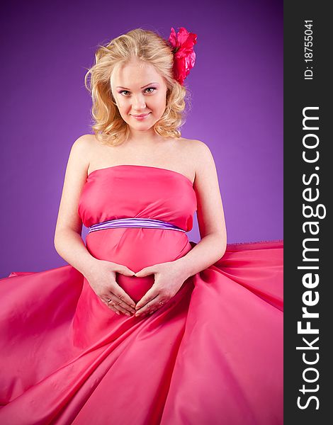 A young pregnant woman in a pink dress on the purple background. A young pregnant woman in a pink dress on the purple background