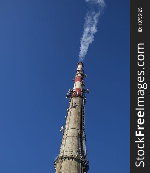A tall chimney with smoke visible against the blue sky