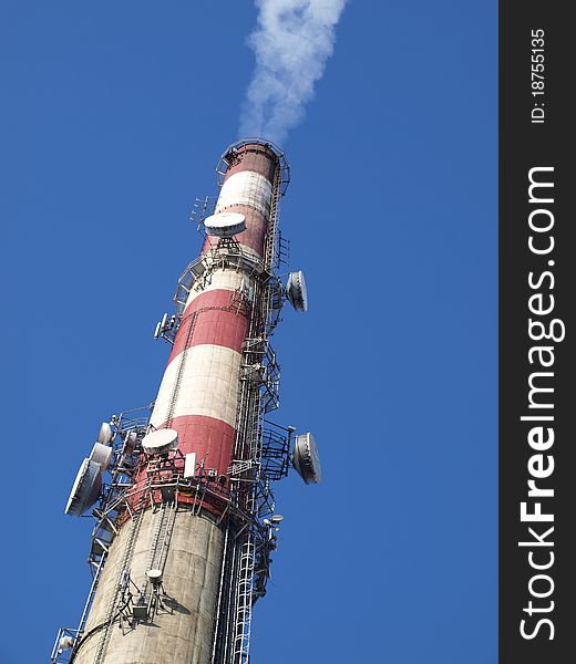 A tall chimney with smoke visible against the blue sky